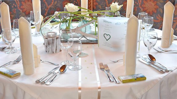 Ein elegant dekorierter Tisch mit weißen Kerzen, Gläsern und Besteck. In der Mitte befindet sich eine Blumendekoration und eine Menükarte. - Hotel Tauferberg - Niederthai