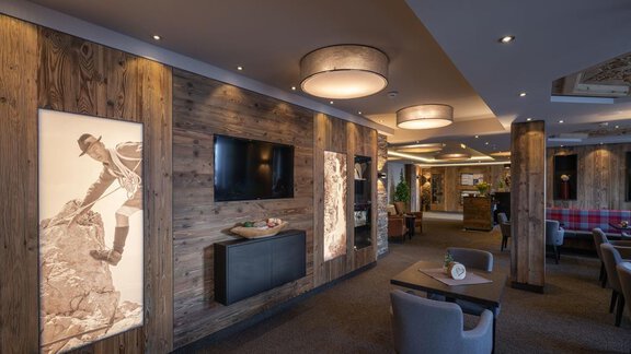 Ein eleganter Innenraum mit Holzverkleidung und modernen Lichtern. An der Wand sind Bilder von Bergsteigern und ein Fernseher zu sehen. - Hotel Tauferberg - Niederthai