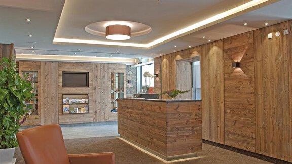 Ein moderner Empfangsbereich mit Holzverkleidung und stilvoller Beleuchtung. Ein Empfangstresen und eine bequeme Sitzecke laden zum Verweilen ein. - Hotel Tauferberg - Niederthai
