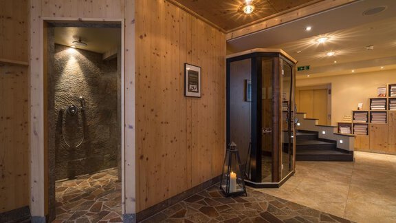 Ein moderner Wellnessbereich mit Holzverkleidung und natürlichem Stein. Auf der linken Seite befindet sich eine Dusche, während auf der rechten Seite eine Sauna zu sehen ist. - Hotel Tauferberg - Niederthai