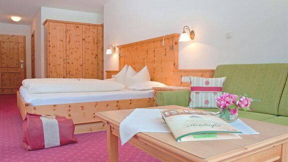 Ein gemütliches Hotelzimmer mit Holzverkleidung und einem Doppelbett. Auf dem Tisch liegt eine Broschüre, und frische Blumen verleihen dem Raum eine einladende Atmosphäre. - Hotel Tauferberg - Niederthai