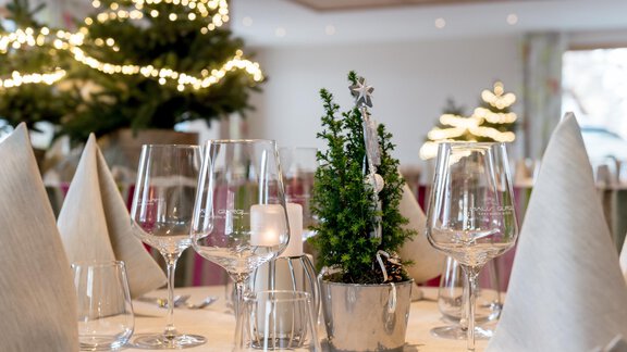 Ein festlich gedeckter Tisch mit Gläsern und einem kleinen Weihnachtsbaum in der Mitte. Im Hintergrund sind weitere dekorierte Weihnachtsbäume zu sehen. - Skihotel Haus Gurgl - Obergurgl 