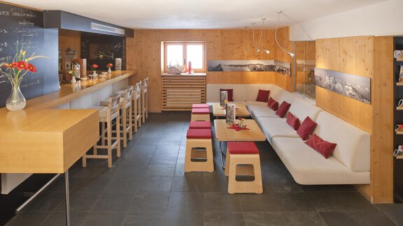 A modern, cozy interior with a long bar and seating options. The walls are made of wood, and there are red accents on the furniture. - Universitätszentrum Obergurgl - Obergurgl 