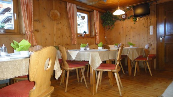 A cozy restaurant with wooden walls and tables. The tables are covered with tablecloths and plants are placed around. - Haus Elisabeth - Vent