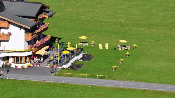 Ein gemütliches Restaurant mit einem großen Außenbereich und bunten Sonnenschirmen. Rasenflächen mit Liegen und Blumenbeeten laden zum Entspannen ein. - Hotel Tauferberg - Niederthai