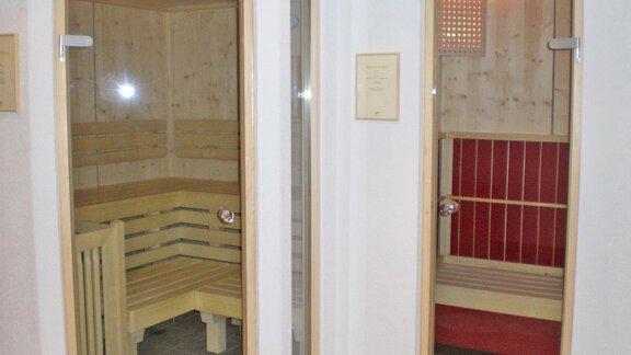 Zwei Saunakabinen in einem Wellnessbereich. Die linke Kabine hat Holzbank und Glasdoor, während die rechte Kabine in Rot gestaltet ist. - Pension Angern - Obergurgl 