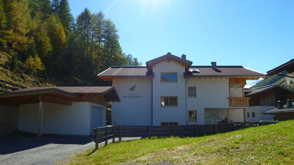 Ein modernes Haus in einer grünen Umgebung, umgeben von Bäumen. Die Sonne scheint hell am klaren Himmel. - Pension Angern - Obergurgl 