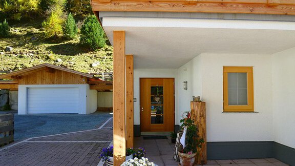 Ein modernes Holzhaus mit einem einladenden Eingang. Im Vordergrund blühen Pflanzen und im Hintergrund sind weitere Gebäude und Bäume zu sehen. - Pension Angern - Obergurgl 