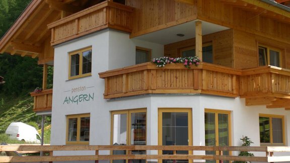 Ein modernes Holzhaus mit mehreren Balkonen und bunten Blumen. Die Fassade ist hell und freundlich, umgeben von grüner Natur. - Pension Angern - Obergurgl 