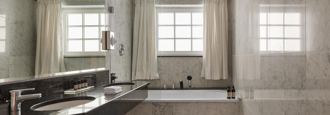 Ein modernes Badezimmer mit marmorierten Wänden und einem eleganten Waschbecken. Die großen Fenster lassen viel Tageslicht hinein. - TOP Hotel Hochgurgl - Hochgurgl