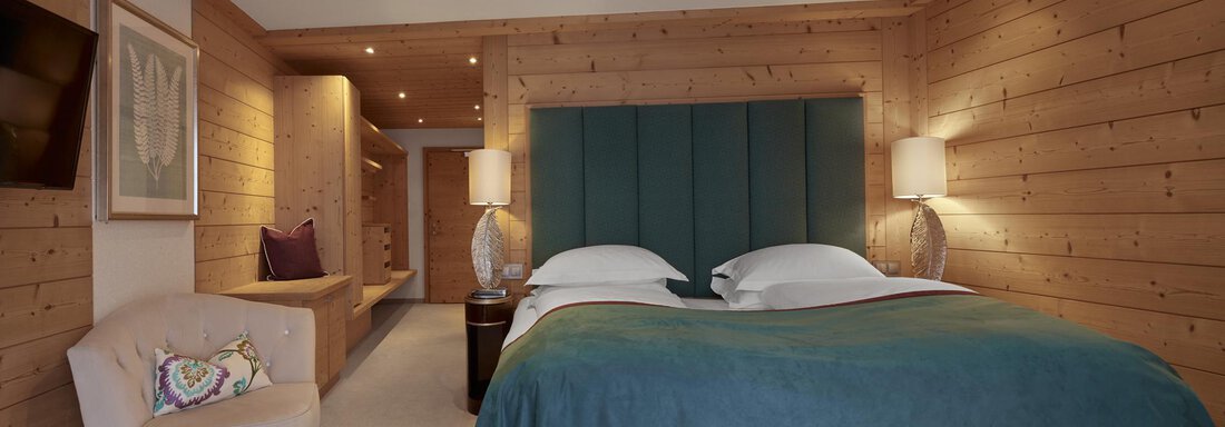 Deluxe Mountain View | © TOP Hotel Hochgurgl (CC C) Ein gemütliches Hotelzimmer mit Holzwänden, einem großen Bett und modernen Lampen. Eine bequeme Sitzecke vervollständigt die angenehme Atmosphäre. - TOP Hotel Hochgurgl - Hochgurgl