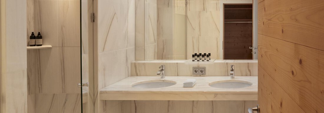 Ein modernes Badezimmer mit stilvollen Waschbecken und großen Spiegeln. Die Wände sind mit hellem, marmoriertem Material gefliest. - TOP Hotel Hochgurgl - Hochgurgl
