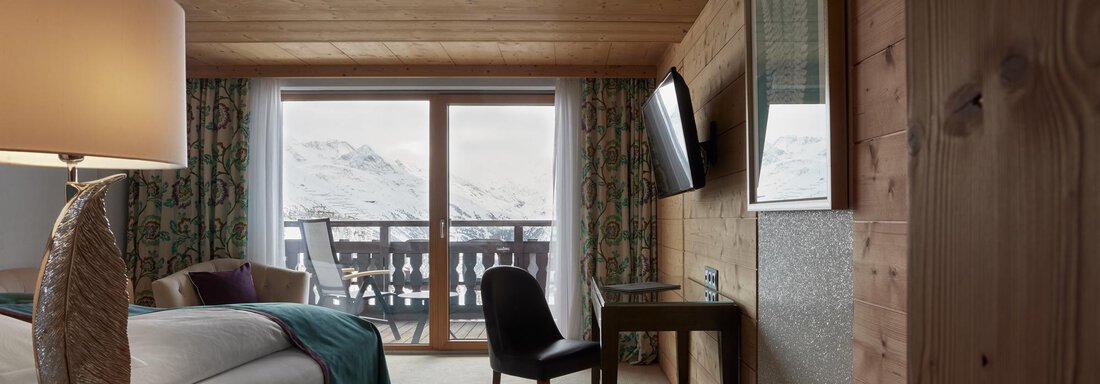 Ein modernes Hotelzimmer mit Holzelementen und einem großen Fenster. Der Blick zeigt einen Balkon mit Aussicht auf die Berge. - TOP Hotel Hochgurgl - Hochgurgl