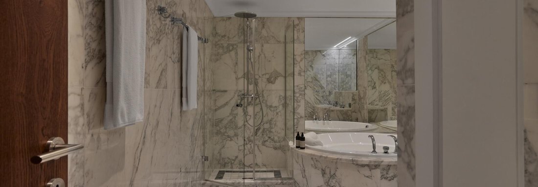 Ein modernes Badezimmer mit eleganten Marmorwänden und einem großen Badewannenbereich. Die Dusche ist klar abgetrennt und es gibt saubere Handtücher. - TOP Hotel Hochgurgl - Hochgurgl