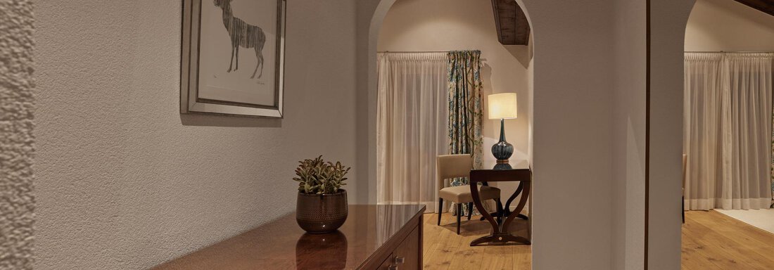Ein gemütlicher Flur mit einem Holzschrank und einem dekorativen Bild an der Wand. Im Hintergrund ist ein Raum mit einer Lampe und einem Tisch sichtbar. - TOP Hotel Hochgurgl - Hochgurgl