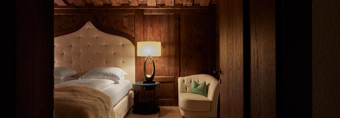 Junior Suiten | © TOP Hotel Hochgurgl (CC C) Ein gemütliches Schlafzimmer mit einem großen Bett und einer hellen Lampe. Die Wände sind aus Holz, und ein bequemer Sessel steht in der Ecke. - TOP Hotel Hochgurgl - Hochgurgl