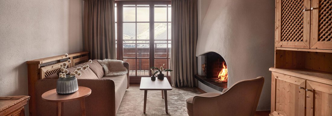 Junior Suite Fireplace Mountain View | © TOP Hotel Hochgurgl (CC C) Ein gemütliches Wohnzimmer mit Holzdecken und einem dekorativen Kamin. Große Fenster lassen viel Tageslicht herein und bieten einen Blick nach draußen. - TOP Hotel Hochgurgl - Hochgurgl