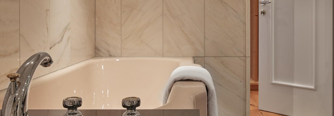 Ein elegantes Badezimmer mit einer freistehenden Badewanne und modernen Armaturen. Die Wände sind mit hellem Marmor verkleidet, und ein Handtuch liegt auf der Badewanne. - TOP Hotel Hochgurgl - Hochgurgl