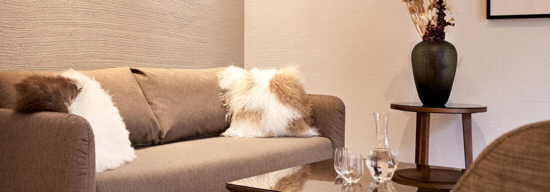 Ein gemütliches Wohnzimmer mit einem beigen Sofa und dekorativen Kissen. Auf dem Tisch stehen Gläser und ein kleiner Tisch mit einer Vase. - TOP Hotel Hochgurgl - Hochgurgl