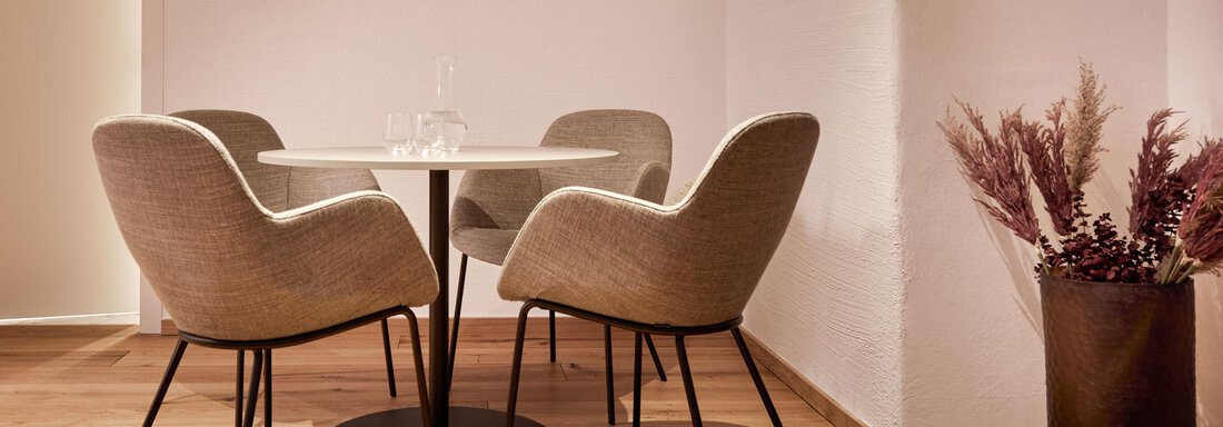 Ein eleganter Raum mit einem runden Tisch und vier gepolsterten Stühlen. Neben dem Tisch steht eine dekorative Pflanze in einem schwarzen Topf. - TOP Hotel Hochgurgl - Hochgurgl