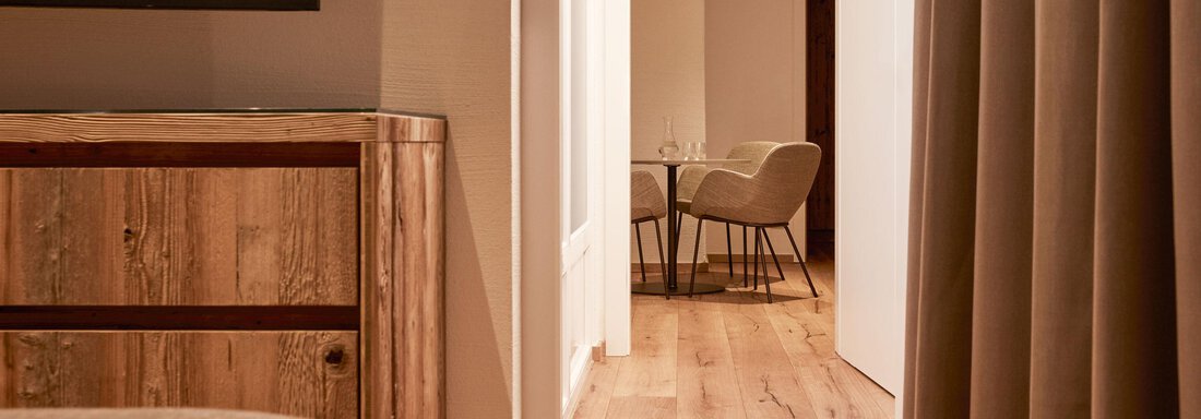Ein gemütliches Zimmer mit einem Holzschrank und einem Fernseher. Im Hintergrund sind ein heller Gang und ein Essbereich sichtbar. - TOP Hotel Hochgurgl - Hochgurgl