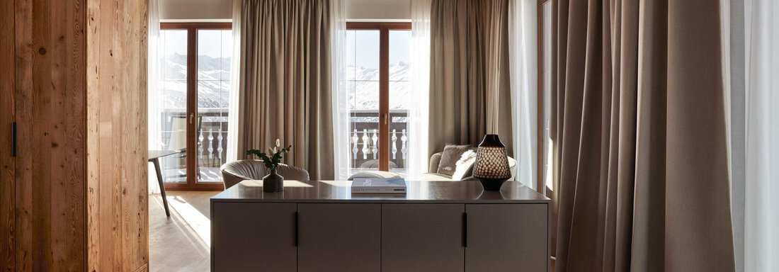 Ein modernes Schlafzimmer mit Holzelementen und großen Fenstern. Die Einrichtung ist schlicht und stilvoll, mit weichen Vorhängen und einem gemütlichen Bett. - TOP Hotel Hochgurgl - Hochgurgl