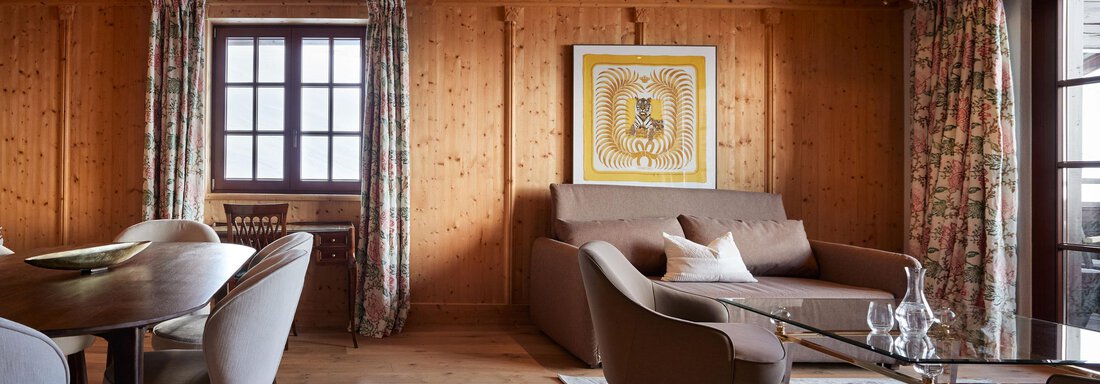 Ein gemütlicher Wohnraum mit Holzwänden und einem modernen Sofa. Es gibt einen Esstisch und große Fenster mit Vorhängen. - TOP Hotel Hochgurgl - Hochgurgl