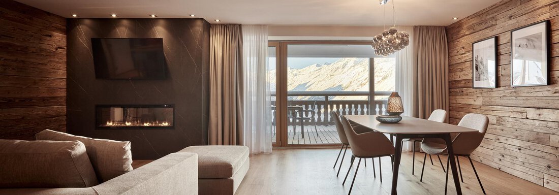 Ein modernes Wohnzimmer mit einem bequemen Sofa und einem Esstisch. Große Fenster bieten einen Blick auf die Berge. - TOP Hotel Hochgurgl - Hochgurgl