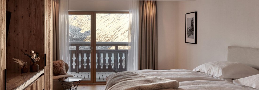 Ein modernes Schlafzimmer mit einem großen Bett und Holzdetails. Große Fenster bieten Ausblick auf die Landschaft. - TOP Hotel Hochgurgl - Hochgurgl