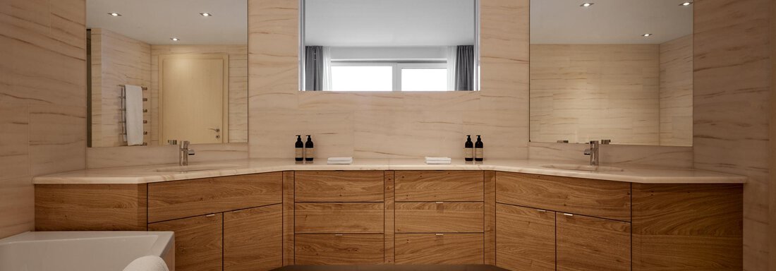 Ein modernes Badezimmer mit hellen Holzschränken und zwei großen Spiegeln. Die Wände sind mit hellen Fliesen gestaltet und der Raum wirkt einladend und geräumig. - TOP Hotel Hochgurgl - Hochgurgl