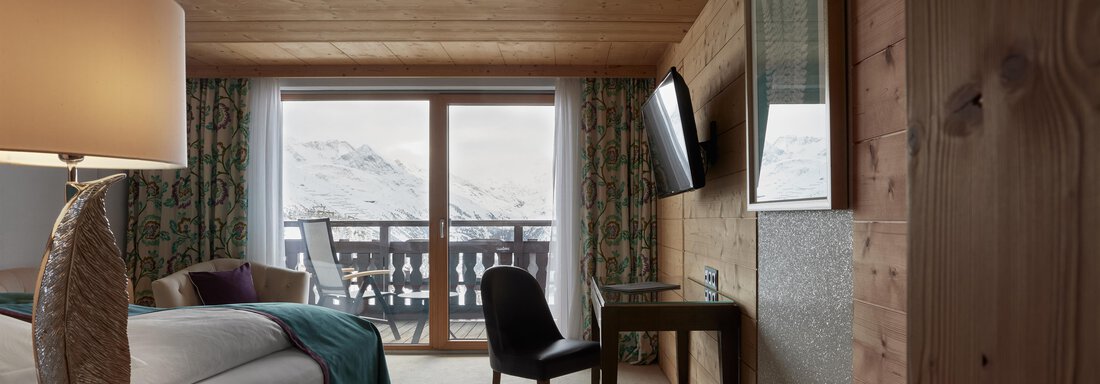 Comfort Room | © Top Hotel Hochgurgl (CC C) Ein modernes Hotelzimmer mit Holzverkleidung und schönem Blick auf die Berge. Es ist gemütlich eingerichtet mit einem Bett, Tisch und einem Stuhl. - TOP Hotel Hochgurgl - Hochgurgl