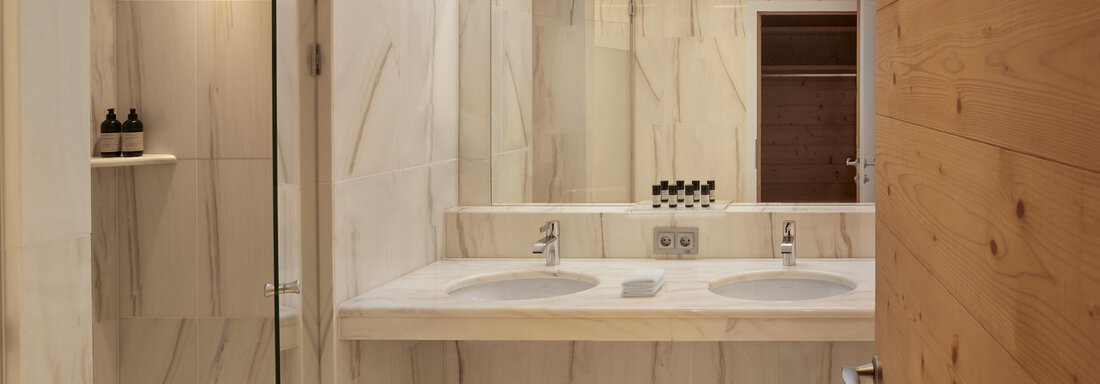 Ein modernes Badezimmer mit hellen Marmormauern und einem großen Spiegel. Es gibt zwei Waschbecken und eine elegante Dusche. - TOP Hotel Hochgurgl - Hochgurgl