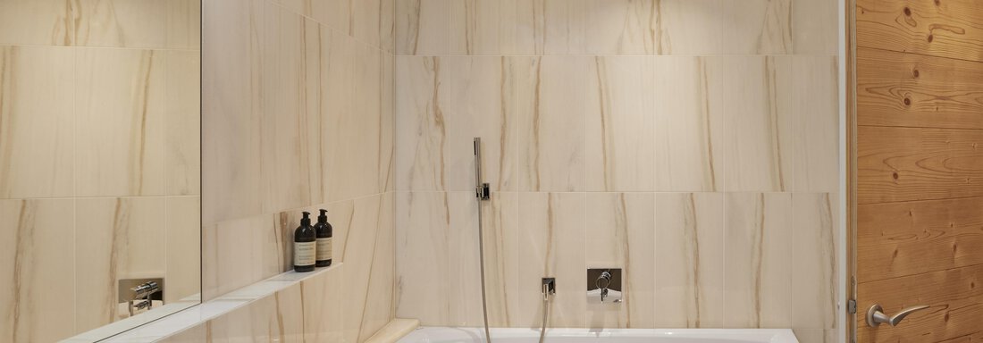 Ein modernes Badezimmer mit einer Badewanne und einer eleganten Wandverkleidung aus Naturstein. Es gibt einen großen Spiegel und eine Holzoberfläche, die eine warme Atmosphäre schafft. - TOP Hotel Hochgurgl - Hochgurgl