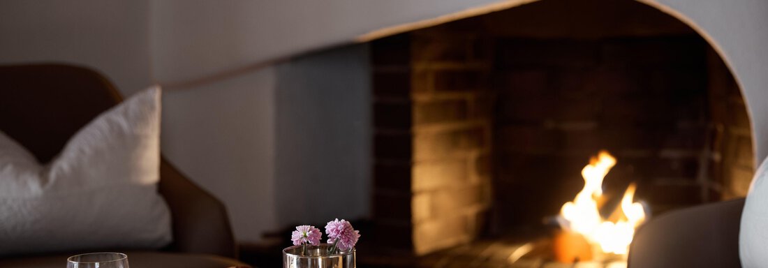 Ein gemütlicher Raum mit einem Kamin und einem Tisch, auf dem zwei Gläser Orangensaft und kleine Leckereien stehen. Im Hintergrund brennt das Feuer im Kamin und sorgt für eine warme Atmosphäre. - TOP Hotel Hochgurgl - Hochgurgl