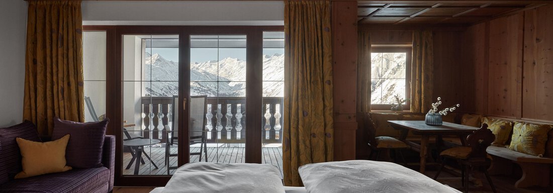 Ein gemütliches Zimmer mit Holzvertäfelung und einem Balkon mit Aussicht auf die Berge. Es gibt ein großes Bett, eine Sitzecke und einen Tisch. - TOP Hotel Hochgurgl - Hochgurgl