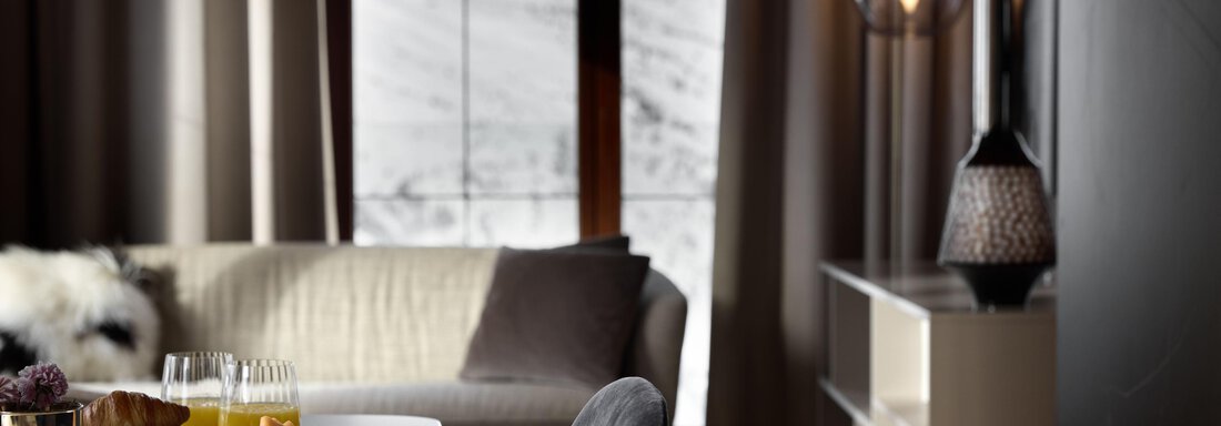 Ein elegantes Wohnzimmer mit einer gemütlichen Couch und schöner Aussicht auf die Berge. Auf dem Tisch stehen Frühstücksgerichte und Getränke. - TOP Hotel Hochgurgl - Hochgurgl