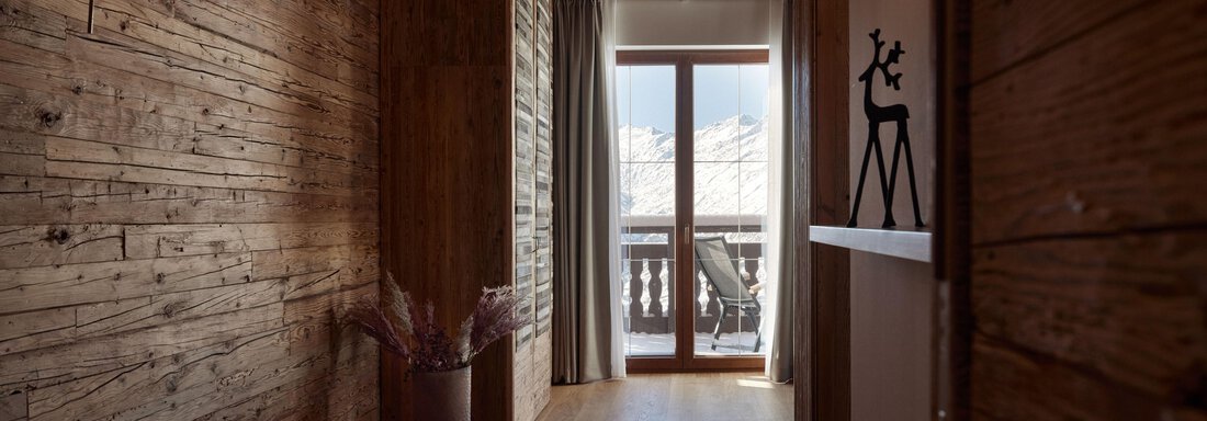 Ein gemütlicher Flur mit Holzverkleidung und sanfter Beleuchtung. Große Fenster bieten einen Blick auf die Berge. - TOP Hotel Hochgurgl - Hochgurgl