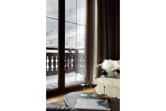 Ein gemütlicher Raum mit Blick auf schneebedeckte Berge. Auf dem Tisch stehen zwei Gläser Wein und ein Buch. - TOP Hotel Hochgurgl - Hochgurgl