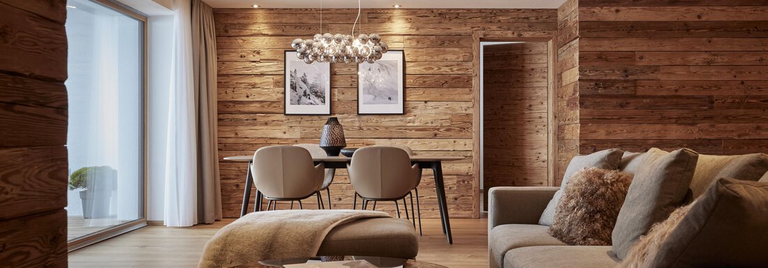 Ein stilvolles Wohnzimmer mit Holzverkleidung und gemütlicher Einrichtung. Ein Esstisch mit Stühlen ist im Vordergrund, während ein Sofa und ein Couchtisch den Raum ergänzen. - TOP Hotel Hochgurgl - Hochgurgl