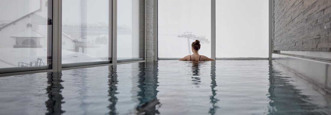 Ein entspannendes Schwimmbad mit einer Person, die im Wasser sitzt. Große Fenster bieten einen Blick auf eine verschneite Landschaft. - TOP Hotel Hochgurgl - Hochgurgl