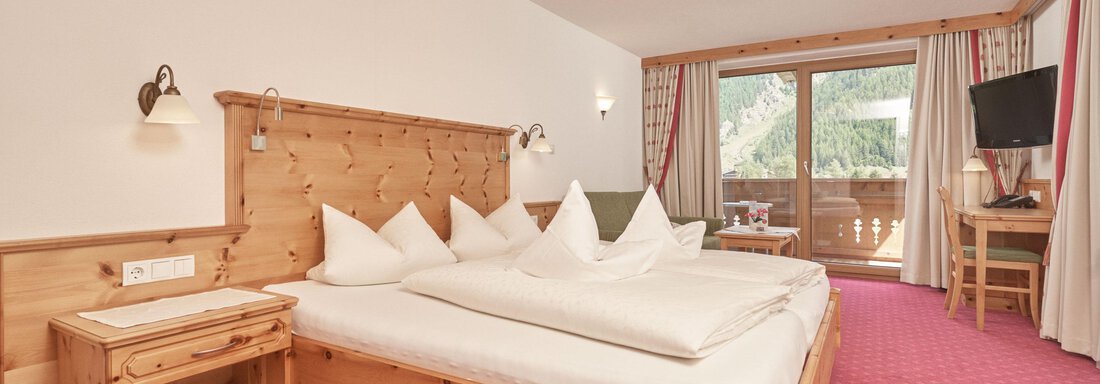 Ein gemütliches Schlafzimmer mit einem Doppelbett und Holzvertäfelung. Große Fenster bieten einen Blick nach draußen und lassen viel Licht herein. - Hotel Tauferberg - Niederthai