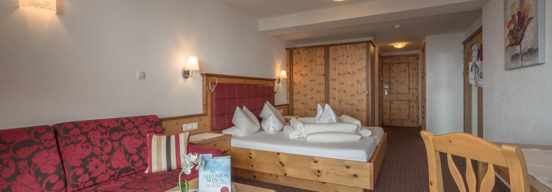 Ein gemütliches Hotelzimmer mit einem Doppelbett und einer roten Couch. Der Raum ist hell und freundlich gestaltet, mit warmen Holzdetails. - Hotel Tauferberg - Niederthai