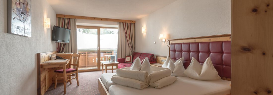 Ein einladendes Hotelzimmer mit einem großen Doppelbett und einer modernen Einrichtung. Der Raum hat einen Balkon und einen kleinen Tisch mit Stühlen. - Hotel Tauferberg - Niederthai