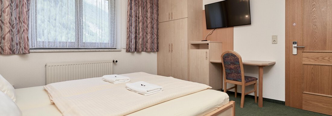 Ein gemütliches Schlafzimmer mit einem Doppelbett und zwei Handtüchern. Der Raum ist hell und modern eingerichtet, mit einem Schreibtisch und einem Fernseher. - Hotel Tauferberg - Niederthai