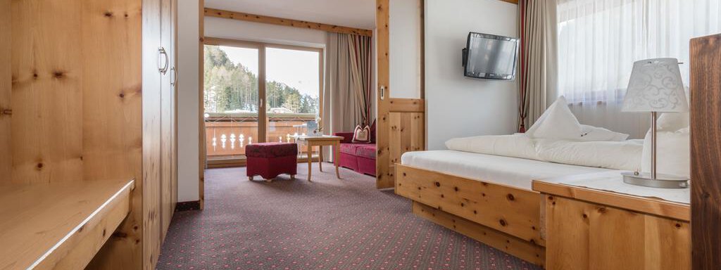 Ein helles Zimmer mit Holzmöbeln und einem gemütlichen Ambiente. Es gibt ein Bett, einen Tisch und einen Fernseher sowie einen Balkon mit Blick auf die Natur. - Hotel Tauferberg - Niederthai