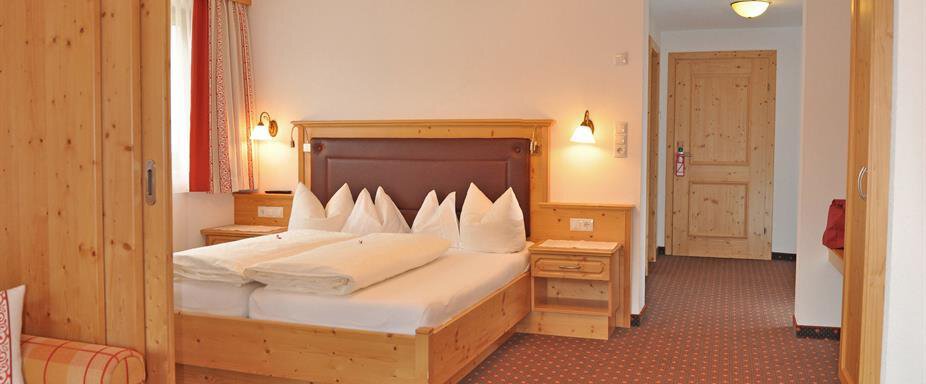 Ein helles Hotelzimmer mit einem großen Doppelbett und gemütlicher Holzverkleidung. Die Sitzecke besteht aus einem Sofa und einem Tisch. - Hotel Tauferberg - Niederthai