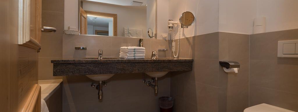 Ein modernes Badezimmer mit einem Doppelwaschbecken und einem großen Spiegel. Die Wände sind in warmen Tönen gehalten und die Ausstattung ist funktional. - Hotel Tauferberg - Niederthai