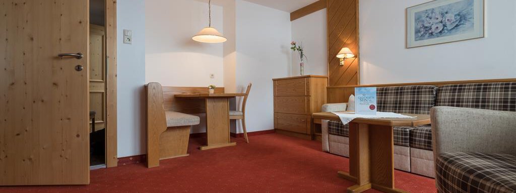 Ein gemütlicher Raum mit rotem Teppich und Holzmöbeln. Es gibt einen Essbereich, ein Sofa und einen kleinen Tisch. - Hotel Tauferberg - Niederthai