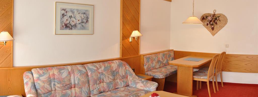 Ein gemütliches Wohnzimmer mit einem farbenfrohen Sofa und einem Tisch. An der Wand hängen dekorative Lichter und ein Bild. - Hotel Tauferberg - Niederthai