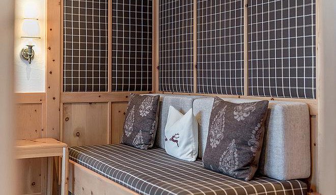 A cozy seating area with a wooden bench and decorative cushions. The walls are designed in a modern grid pattern. - Art & Relax Hotel Bergwelt - Obergurgl 